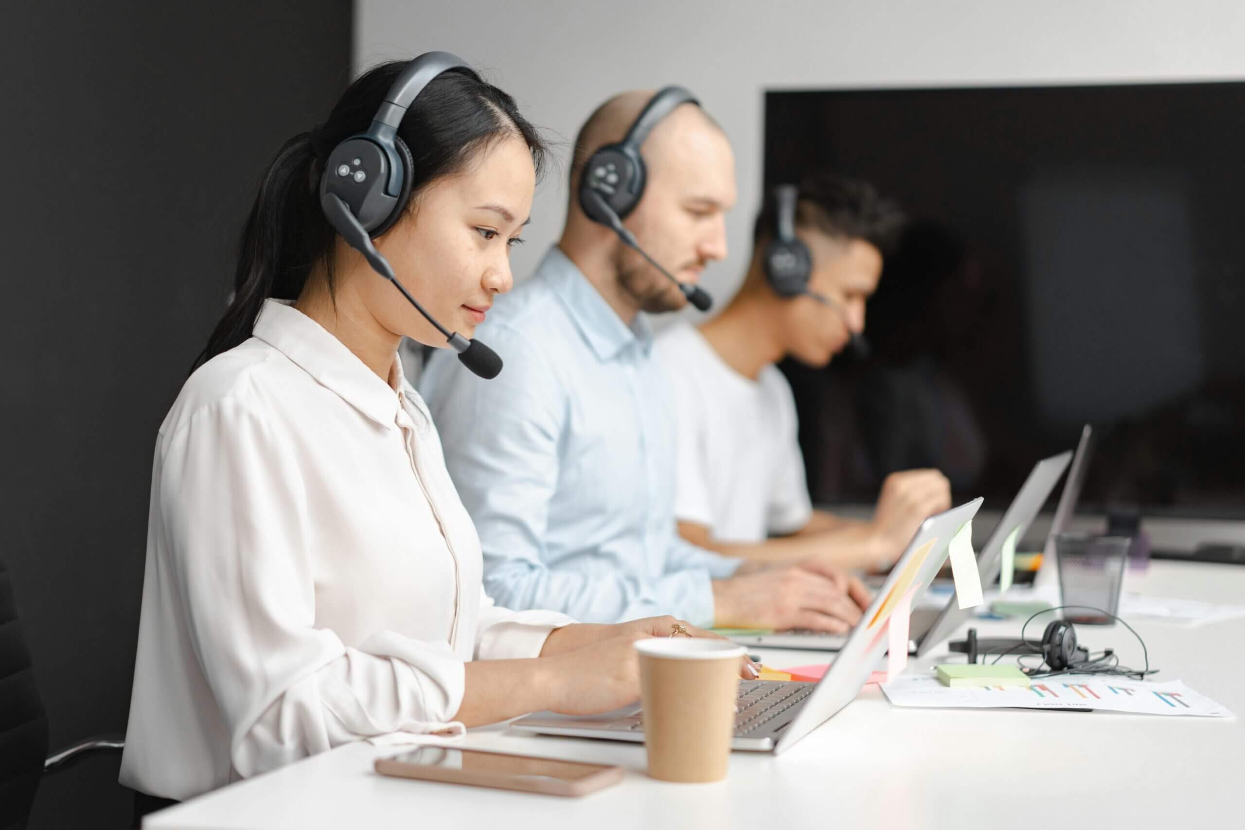 Customer support team working on laptops with headsets in an office.