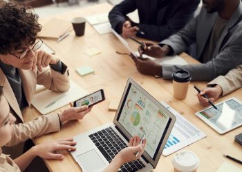 Business team analyzing financial data on laptops and tablets during a meeting.