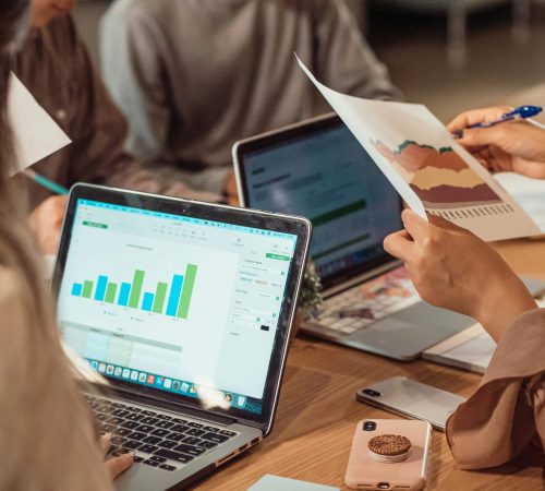 People analyzing financial data on laptops and papers during a meeting.