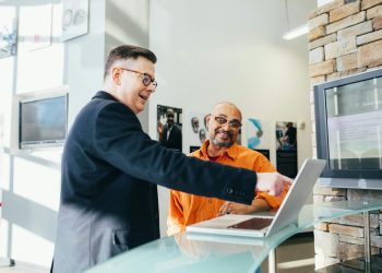 Two businessmen having a lively discussion in a modern office setting, pointing at a laptop screen.