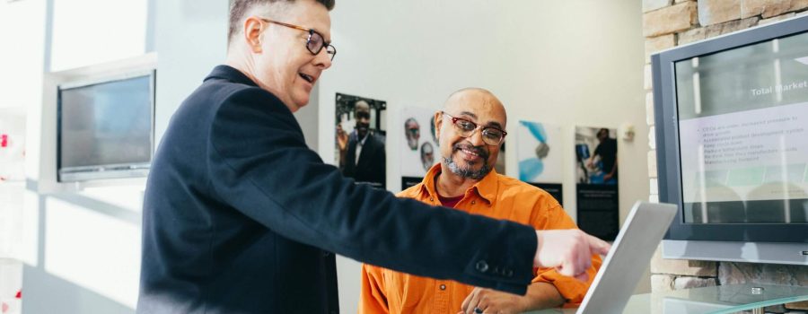 Two businessmen having a lively discussion in a modern office setting, pointing at a laptop screen.