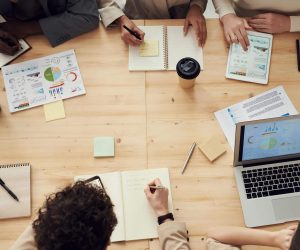 Business professionals in a collaborative team meeting, discussing charts and plans with laptops and notebooks.