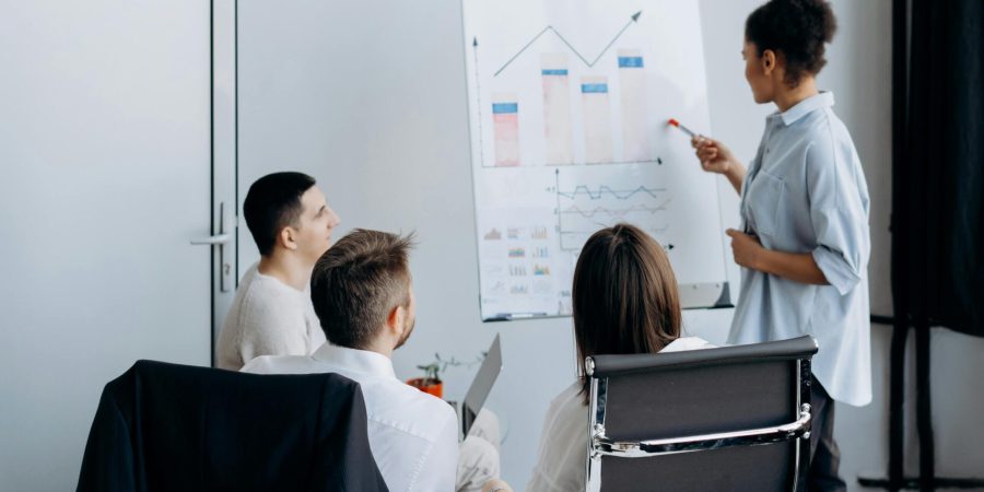 Business team in meeting with presenter discussing charts on a flip board.