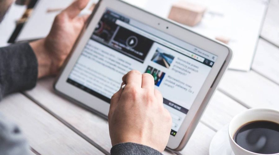 Person using a tablet with a stylus at a table next to a coffee cup.